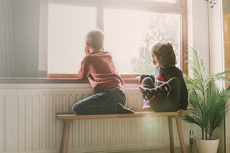 Zwei Kinder sitzen auf einer Bank vor der Heizung und schauen aus dem Fenster