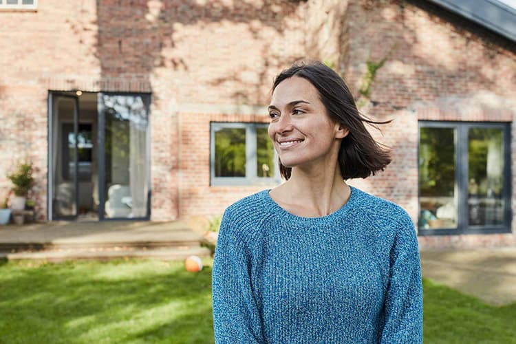Lächelnde Frau im Garten vor einem Wohnhaus