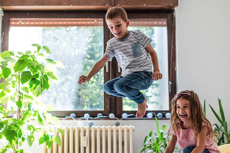 Zwei Kinder turnen und springen im Zimmer vor einer Heizung