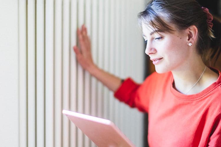 Frau schaut auf ihr Tablet und fühlt die Temperatur der Heizung