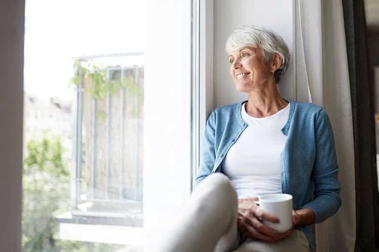 Frau mittleren Alters sitzt auf der Fensterbank und schaut raus