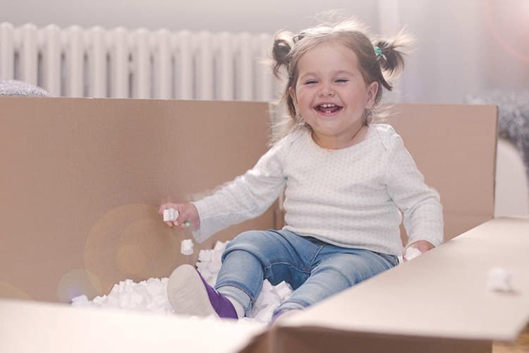 Mädchen sitzt in Umzugskarton vor einer Heizung