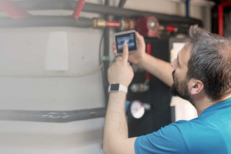 Mann mit Bart schaut auf einen Bildschirm an der Heizungsanlage