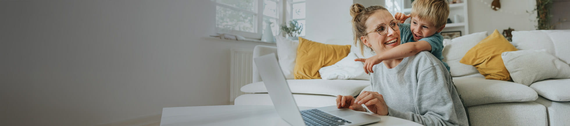 Mutter und Vater sitzen mit zwei Kindern inmitten vieler Pflanzen in ihrem Wohnzimmer und schauen auf einen Laptop