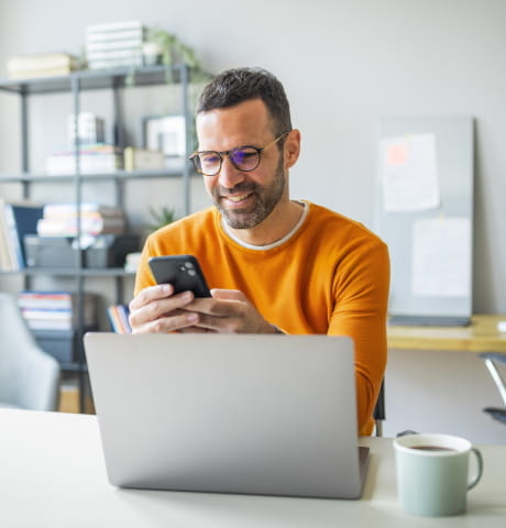 Mann schaut zufriedem auf Laptop und Smartphone