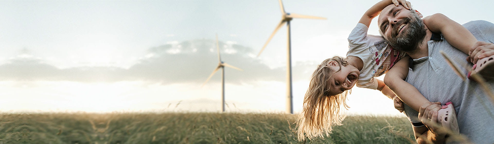 Familienvater mit fröhlichem Kind vor Windrädern, die Energie produzieren, die Sie per dynamischem Strom bon EWE zum Börsenpreis erhalten.