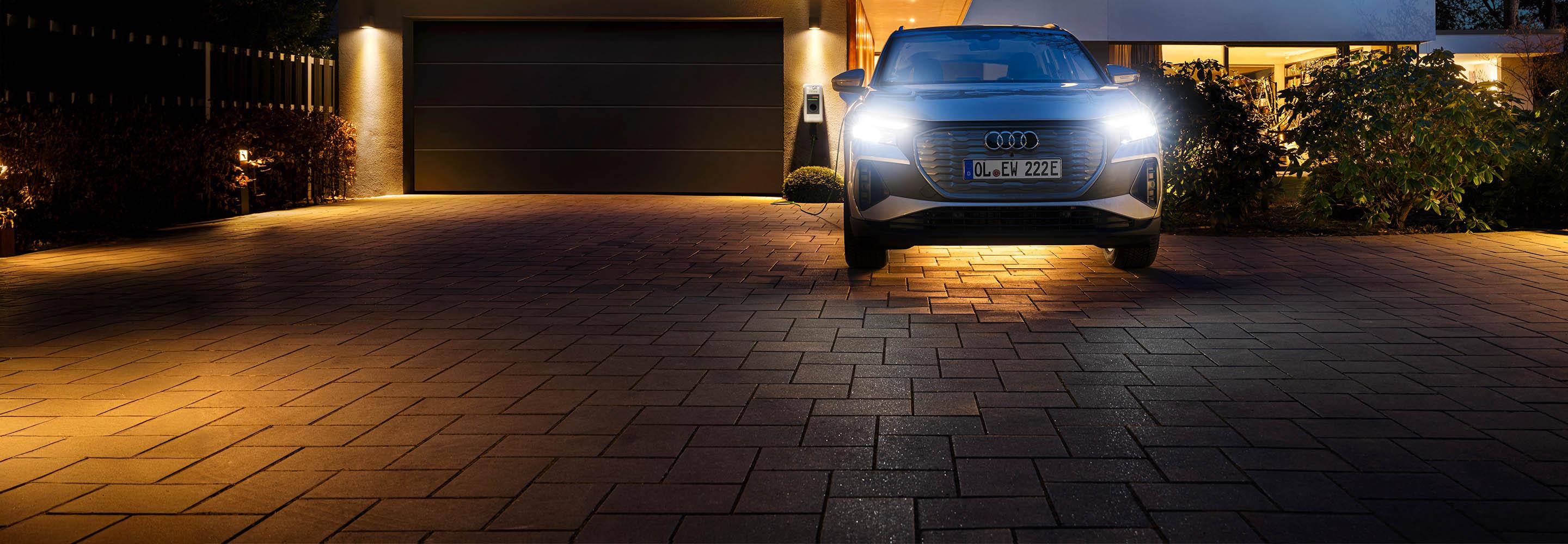 Auto vor einem Haus mit Wallbox im Hintergrund.