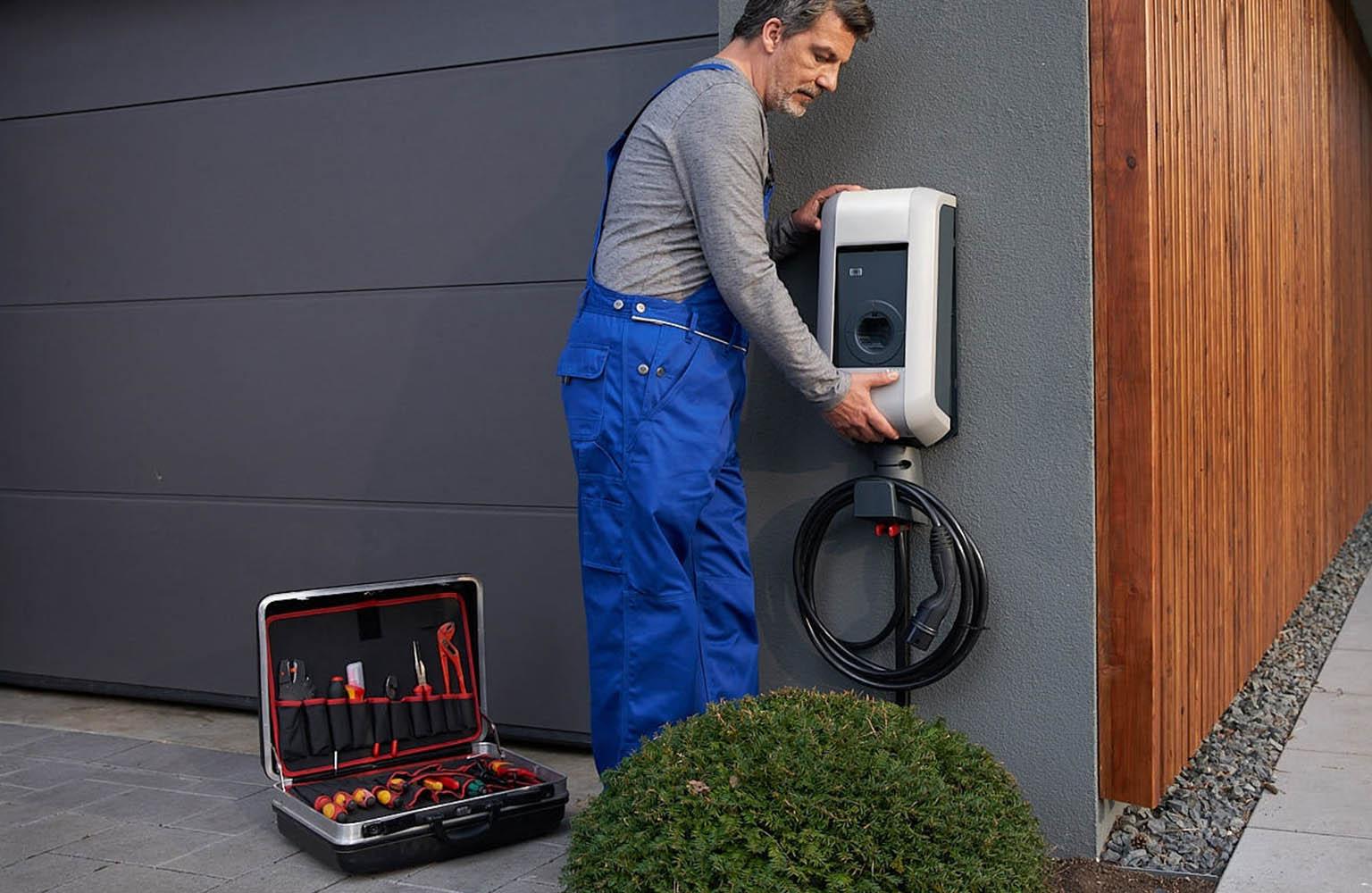 Handwerker bringt Wallbox an Hauswand an.