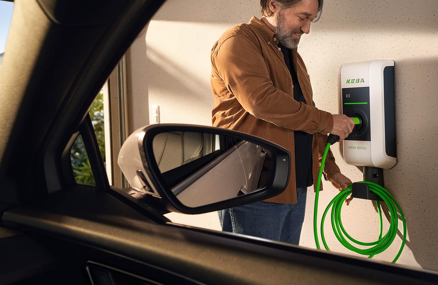 Mann lädt sein Elektroauto an einer Wallbox mit einem grünen Kabel