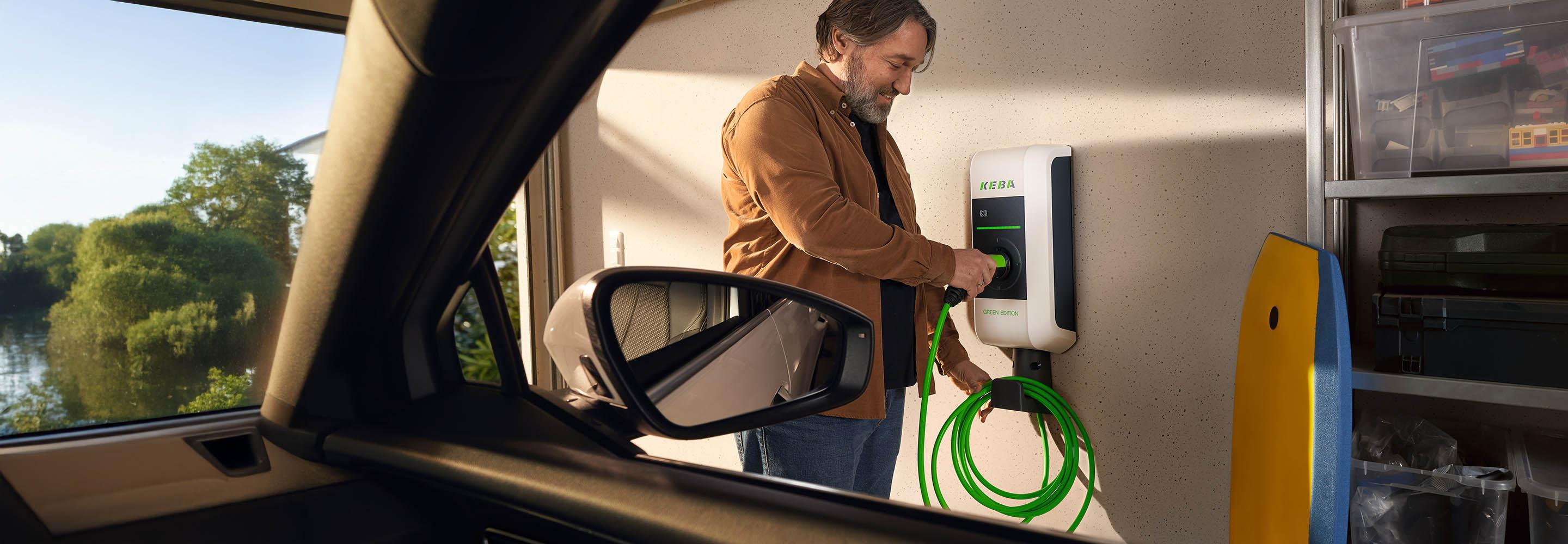 Mann lädt sein Elektroauto an einer Wallbox mit einem grünen Kabel