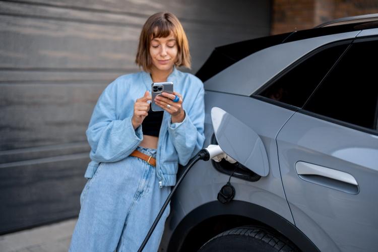 Eine Frau lädt ihr E-Auto und schaut auf ihr Smartphone