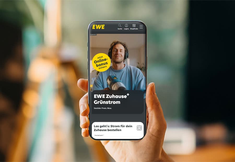 Hand hält Smartphone auf dem der EWE Zuhause+ Grünstrom Tarif zu sehen ist