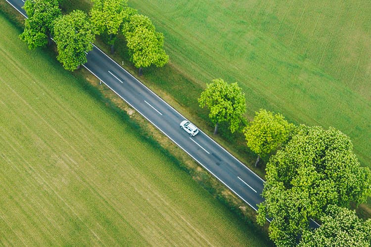 Auto auf einer Landstraße zwischen Feldern aus Vogelperspektive.