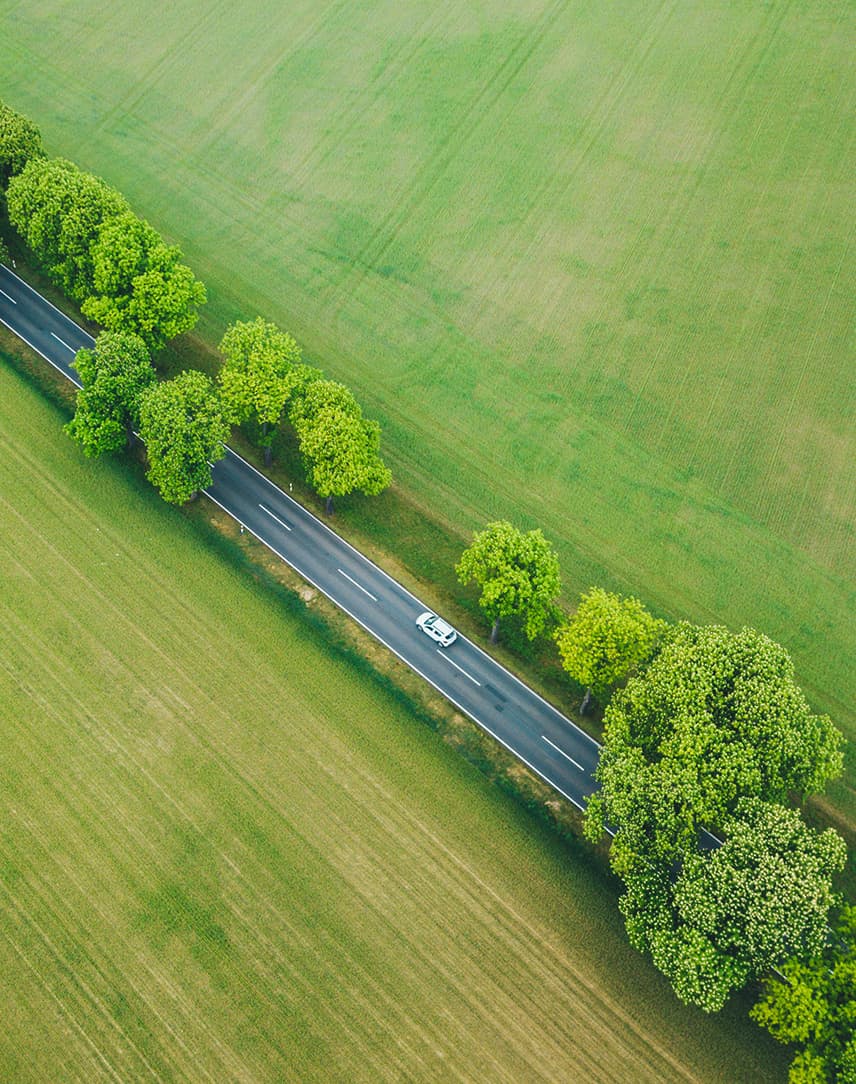 Auto auf einer Landstraße zwischen Feldern aus Vogelperspektive.