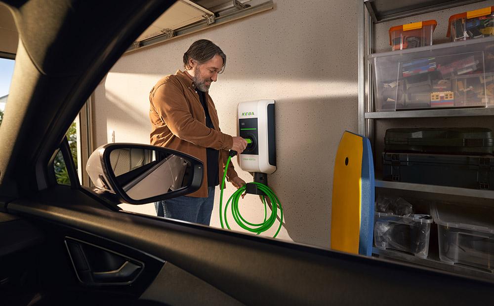 Mann lädt sein Elektroauto an einer Wallbox mit einem grünen Kabel