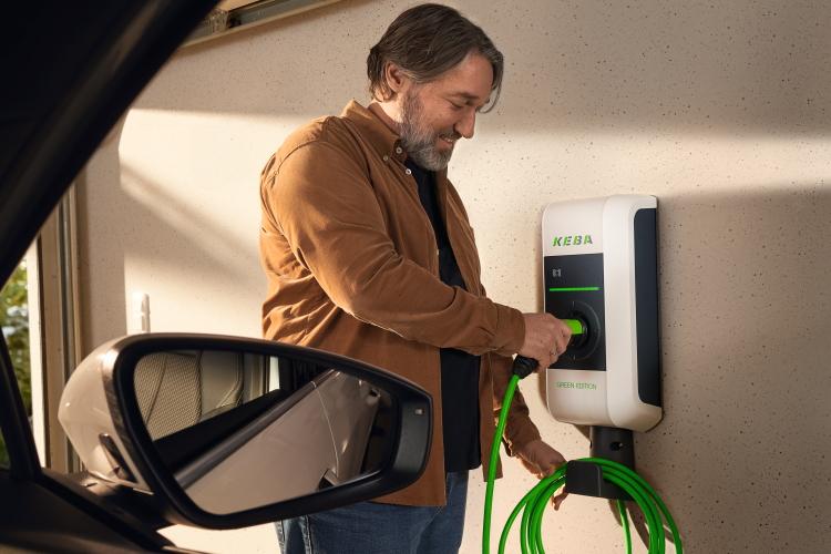 Mann lädt sein Elektroauto an einer Wallbox mit einem grünen Kabel