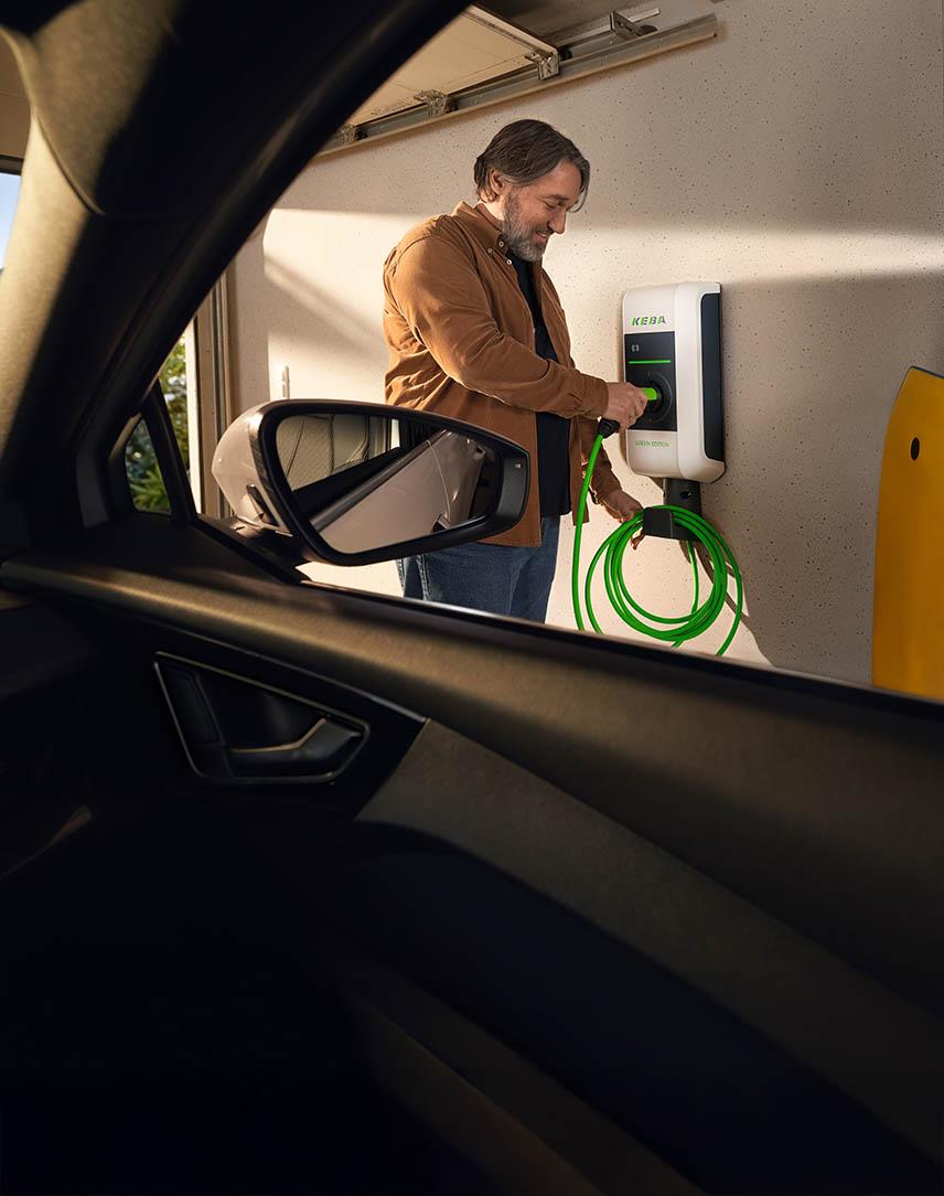 Mann lädt sein Elektroauto an einer Wallbox mit einem grünen Kabel