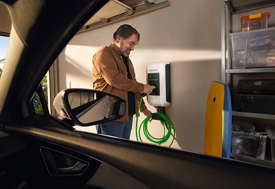 Mann lädt sein Elektroauto an einer Wallbox mit einem grünen Kabel