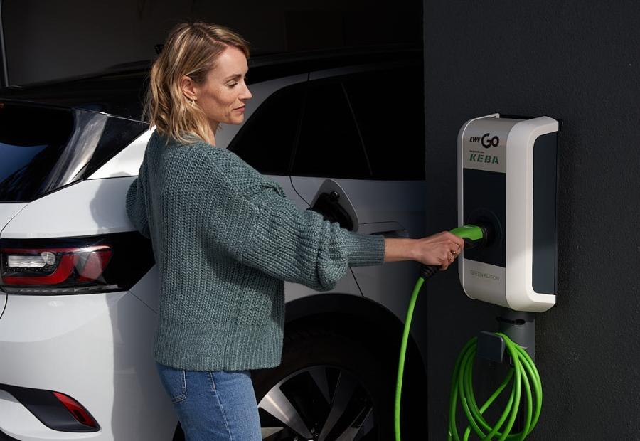 Frau bedient Wallbox an Hauswand neben einem E-Auto.