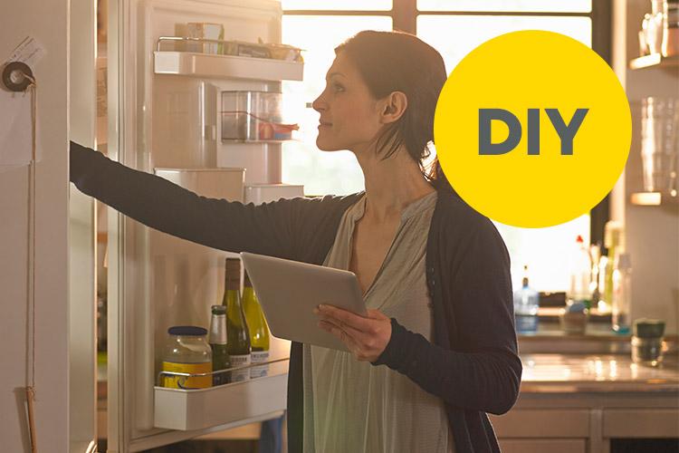 Frau mit Tablet in der Hand greift in den Kühlschrank