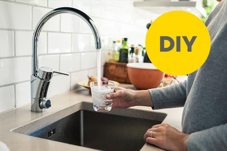 Frau hält Glas unter den laufenden Küchenwasserhahn.