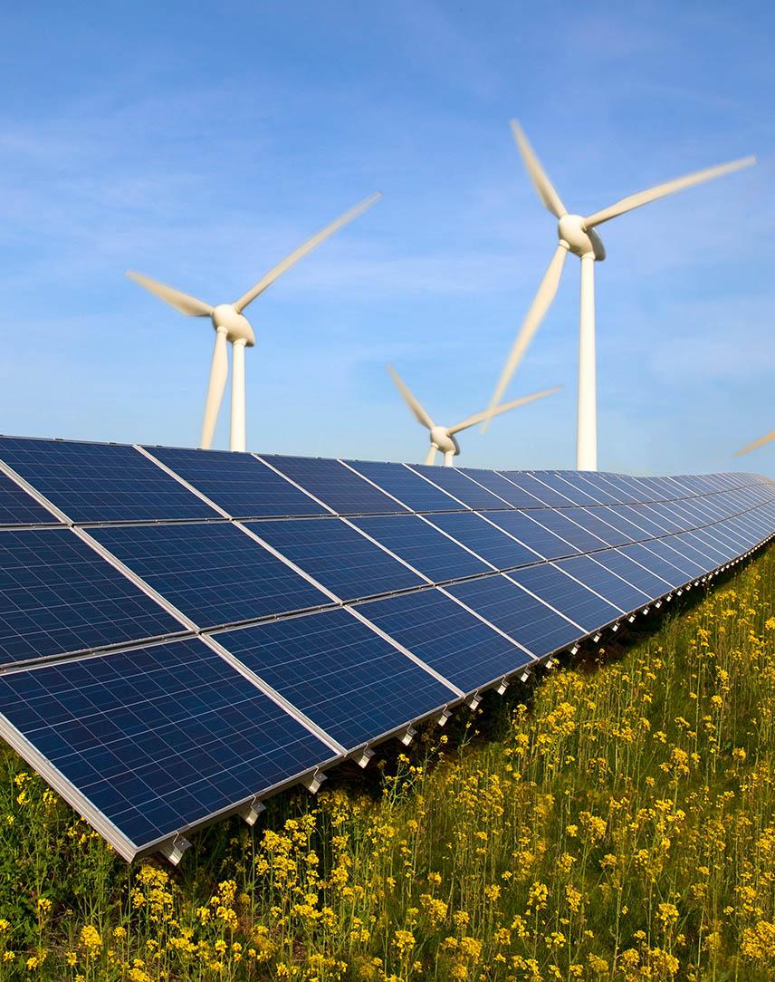 Im Vordergrund sieht man Solarmodule, im Hintergrund Windräder vor blauem Himmel