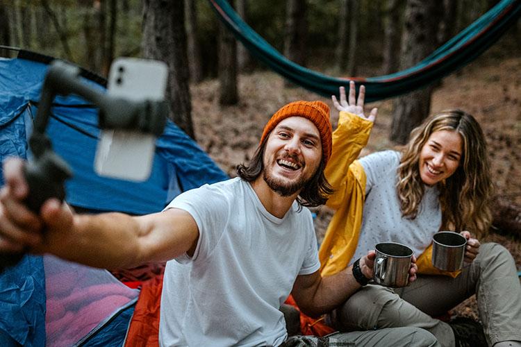 Mann und Frau fotografieren sich beim Campen mit Smartphone im Selfiestick