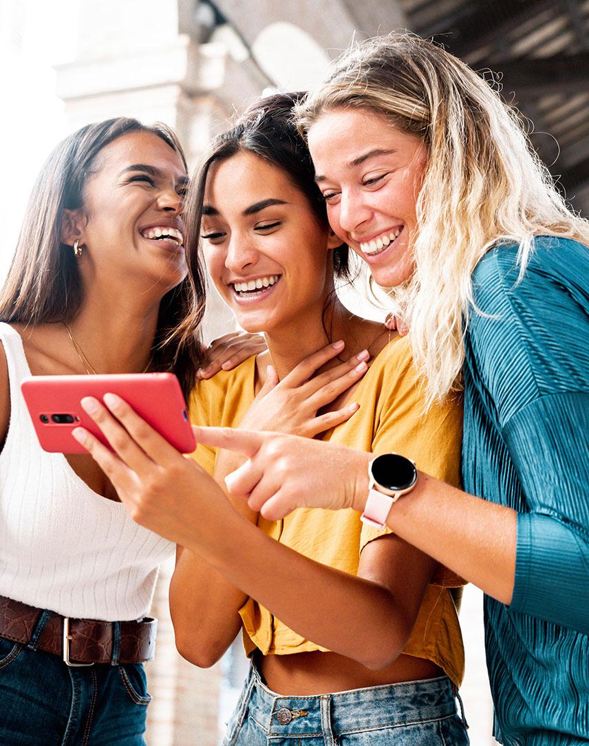 Drei Frauen schauen lachend auf ein Smartphone