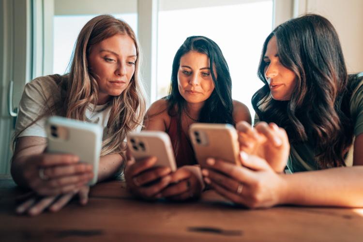 Drei Frauen schauen auf ihr iOS- bzw. Android-Handy