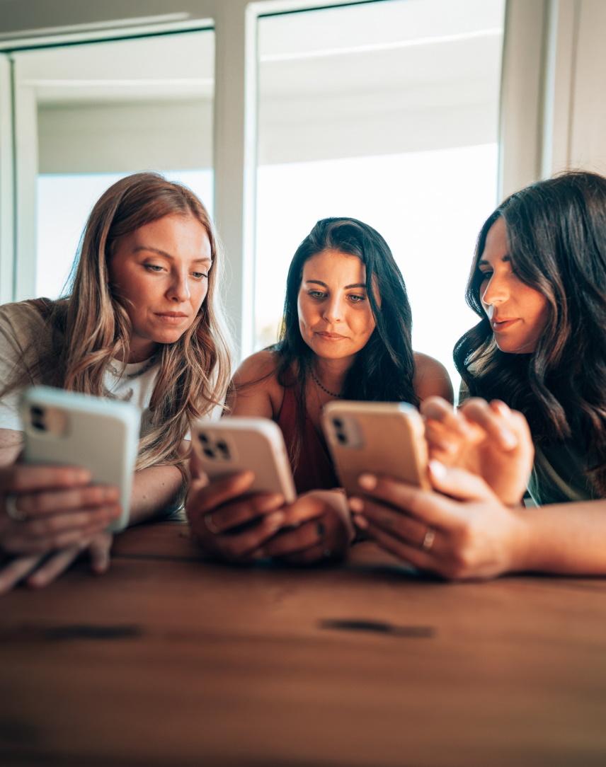 Drei Frauen schauen auf ihr iOS- bzw. Android-Handy