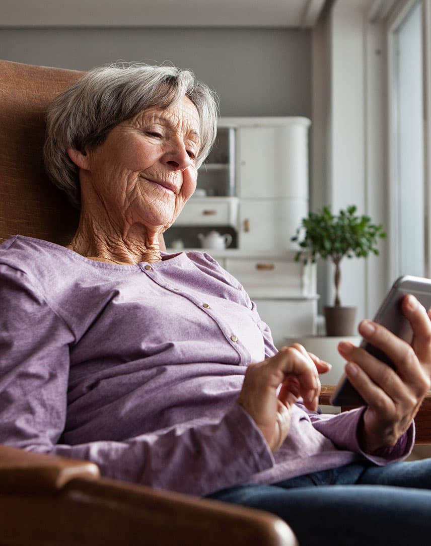 Ältere Frau im Sessel tippt auf Smartphone