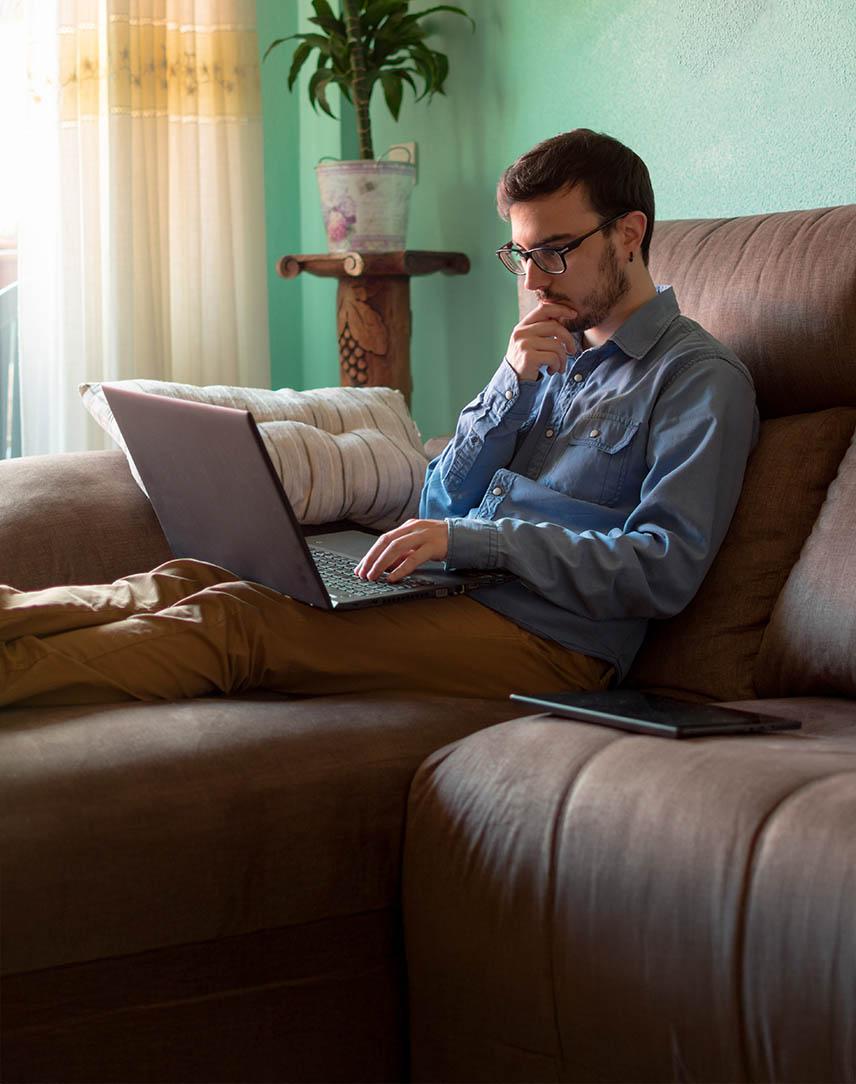 Mann sitzt auf der Couch mit Laptop und informiert sich 