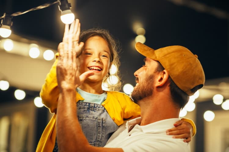 Ein Vater hält sein Kind auf dem Arm, im Hintergrund leuchtet eine Lichterkette