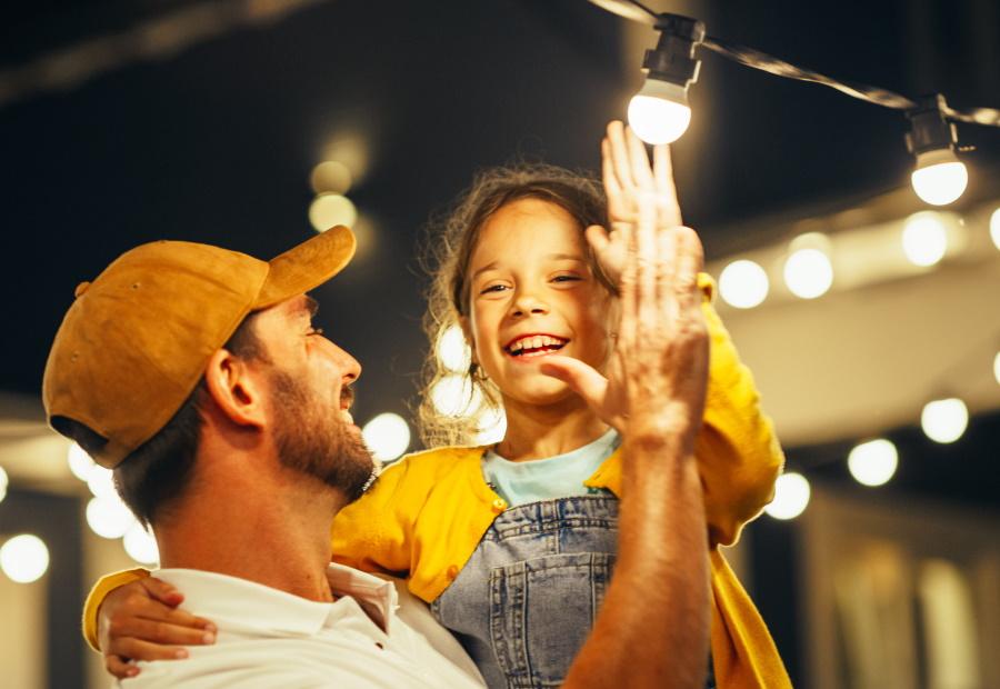Ein Vater hält sein Kind auf dem Arm, im Hintergrund leuchtet eine Lichterkette