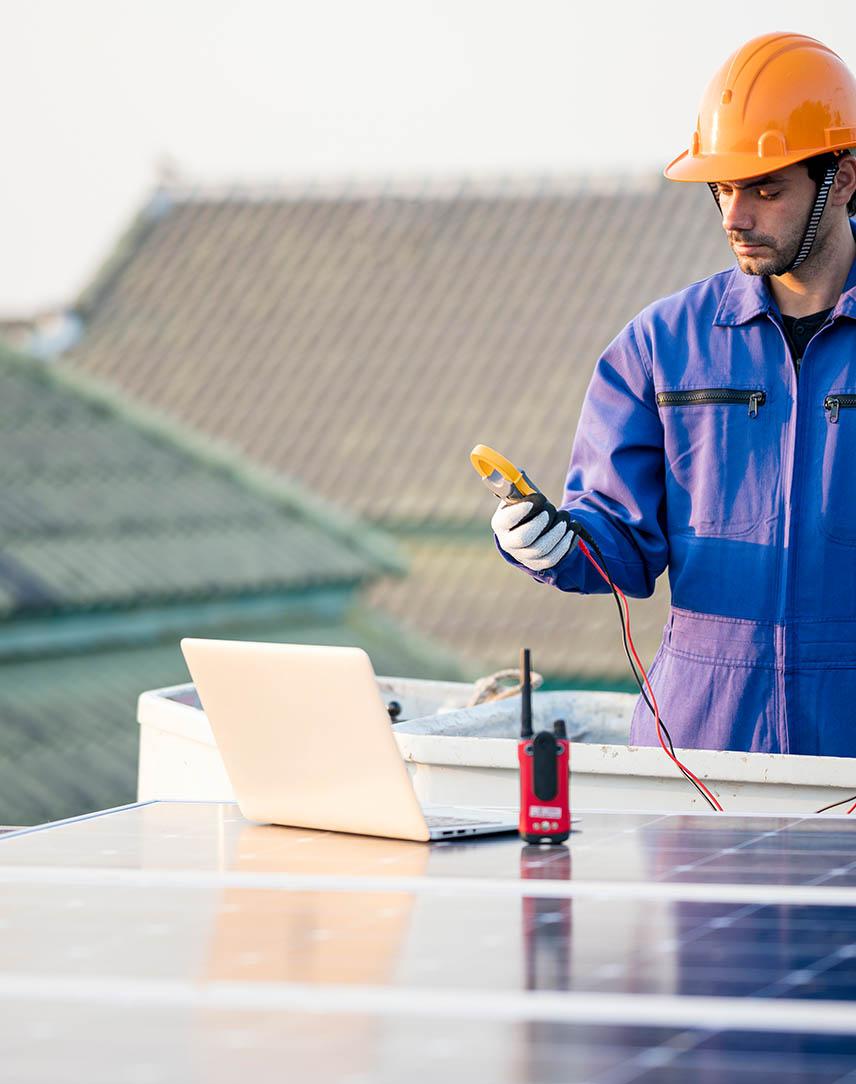 Mann mit Helm prüft die Leistung eines PV-Moduls auf Dach