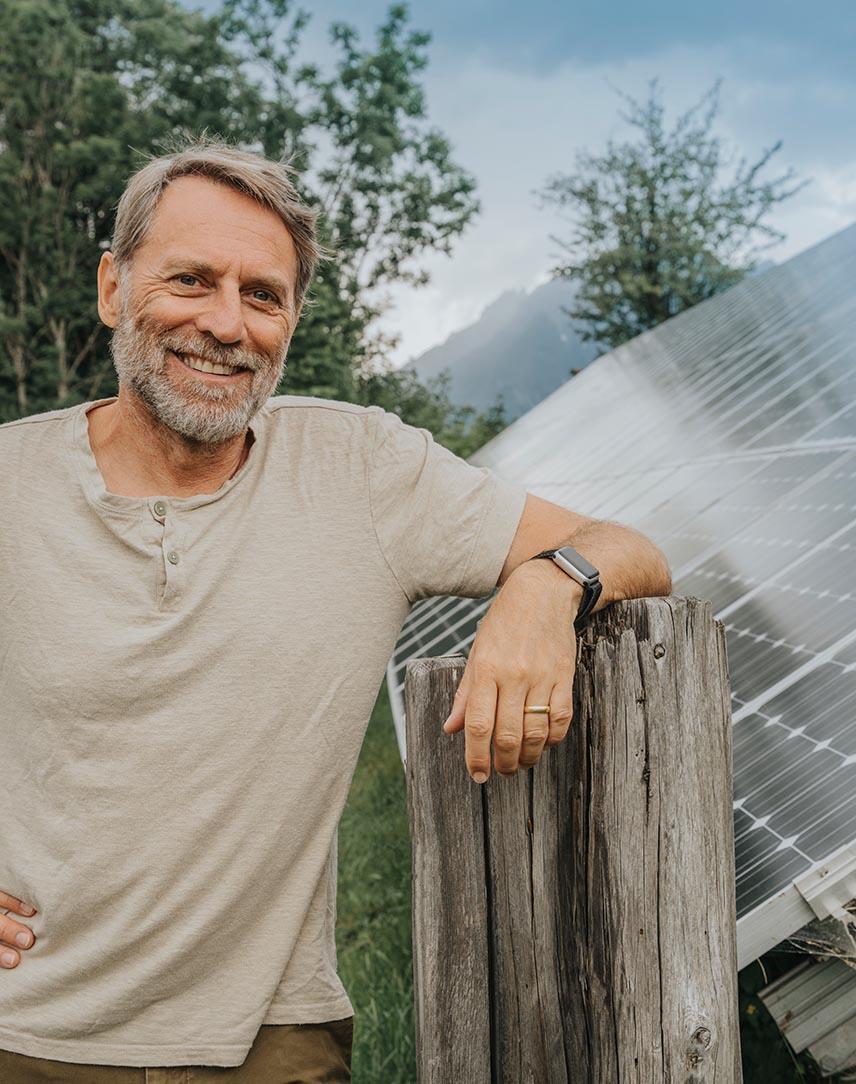 Mann lehnt an Zaun, dahinter ein PV-Modul