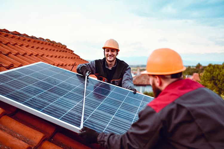 Zwei Männer mit Helm montieren PV-Modul auf einem Dach