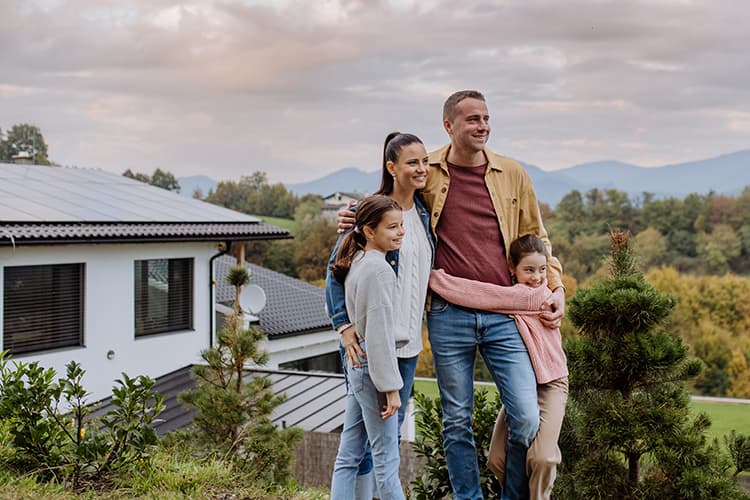 Familie steht vor einem Haus auf dem eine PV-Anlage angebracht ist