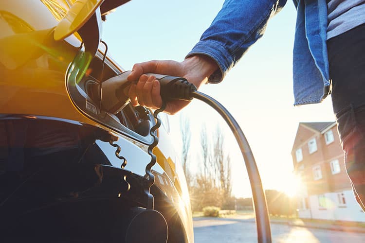 Hand steckt Ladekabel in ein gelbes Elektroauto bei Sonnenuntergang
