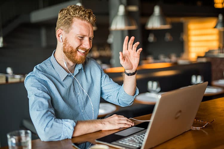 Mann mit Kopfhörern winkt im Café in Laptop-Kamera