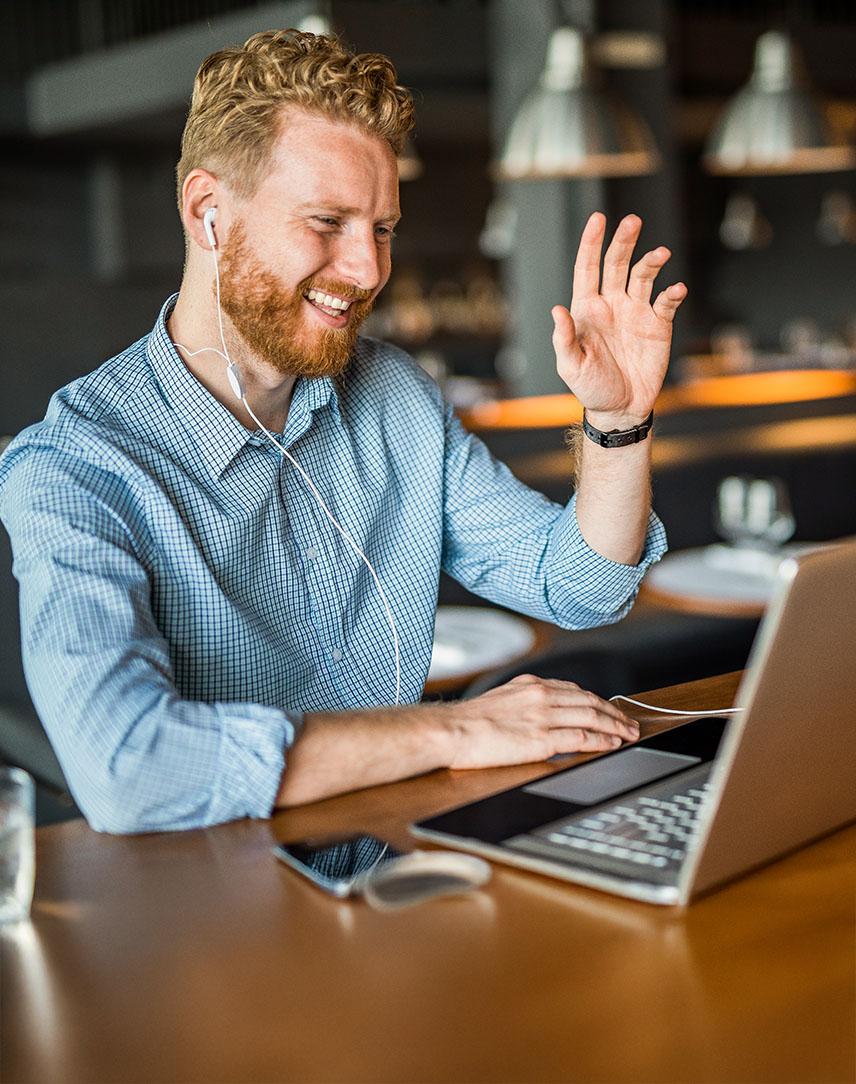 Mann mit Kopfhörern winkt im Café in Laptop-Kamera