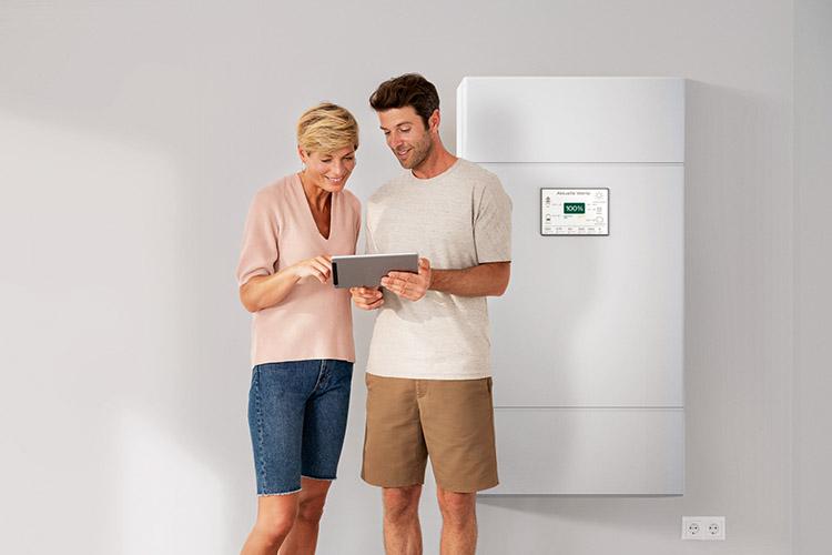 Ein Mann und eine Frau schauen gemeinsam auf ein Tablet vor einem PV-Speicher.