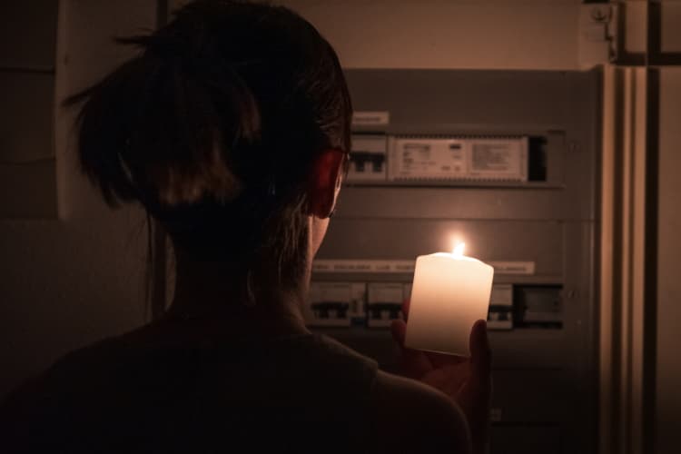 Eine Frau steht im Dunkeln vor ihrem Sicherungskasten und hat eine Kerze in der Hand
