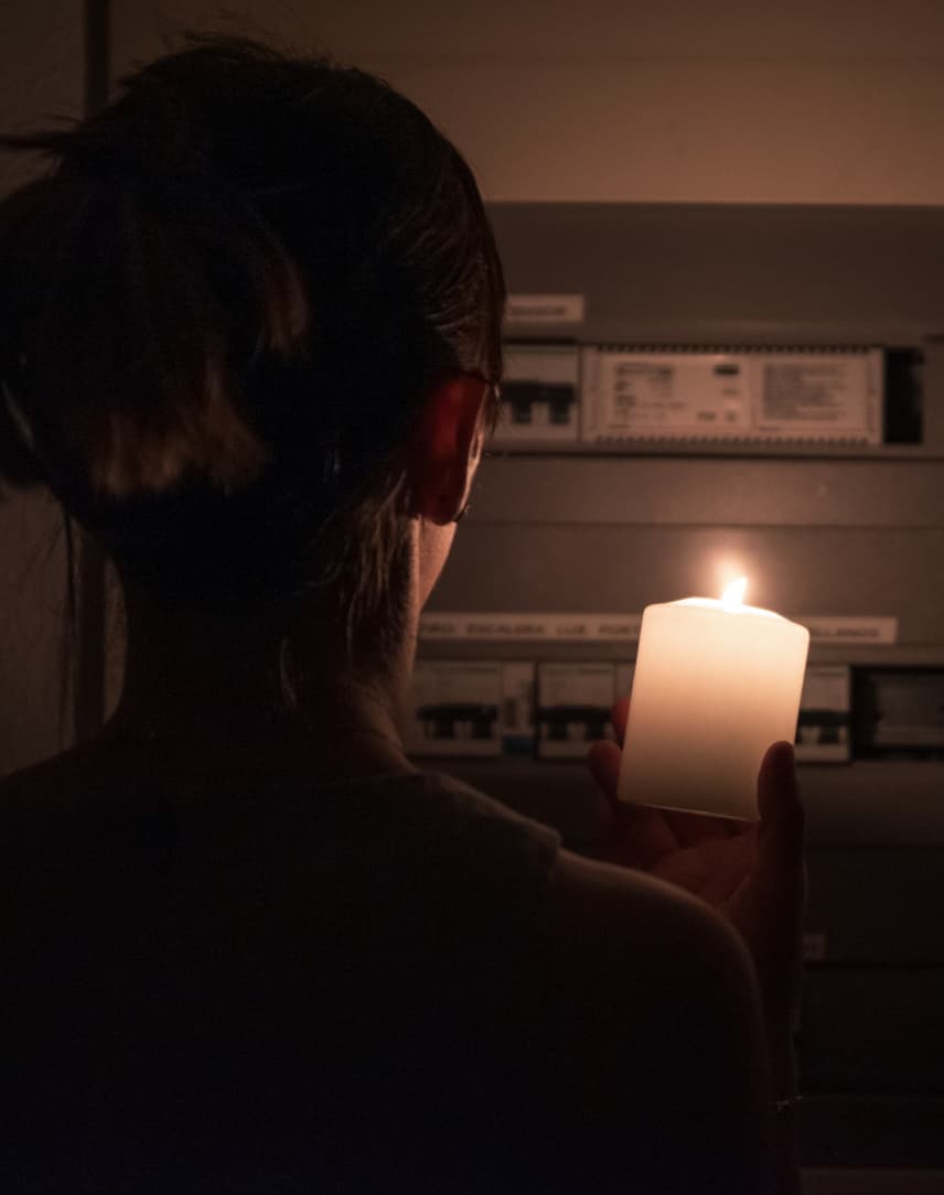Eine Frau steht im Dunkeln vor ihrem Sicherungskasten und hat eine Kerze in der Hand