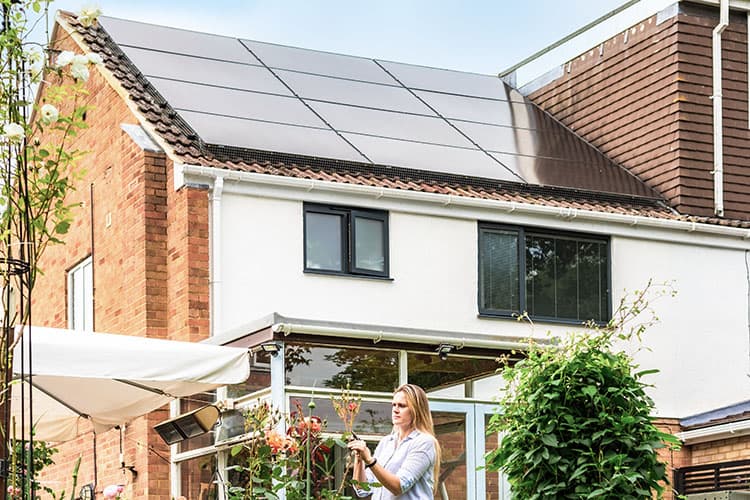 Frau steht im Garten vor einem Haus mit Solarmodulen auf dem Dach