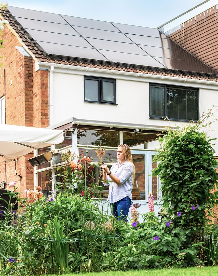 Frau steht im Garten vor einem Haus mit Solarmodulen auf dem Dach