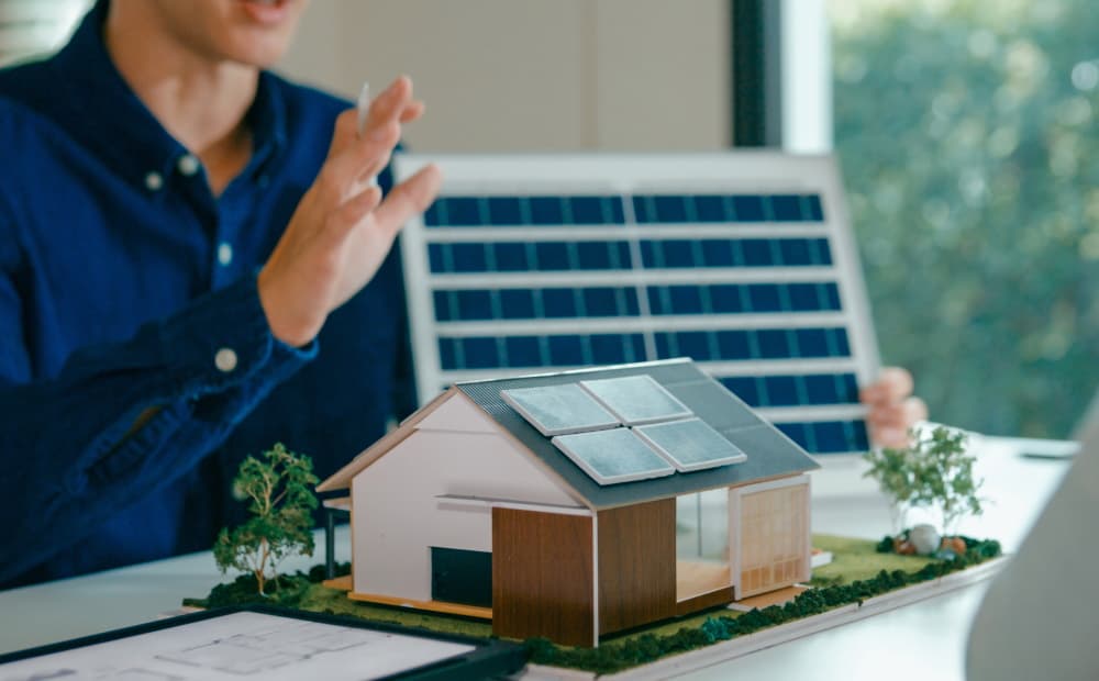 Hausmodell und zwei Personen im Hintergrund die eine PV-Anlage planen