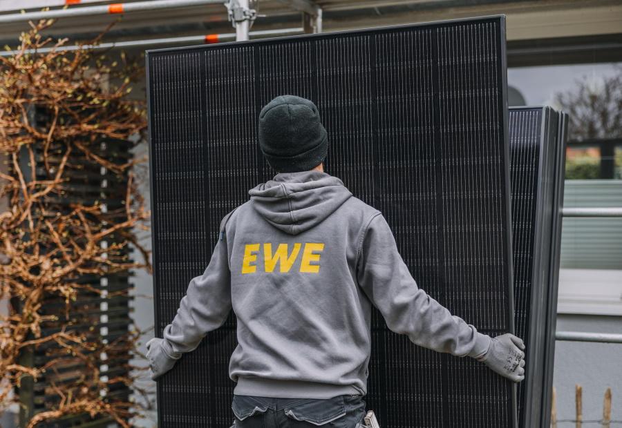 EWE-Mitarbeiter trägt ein PV-Modul der Anlage von EWE-Solarkundin Kerstin