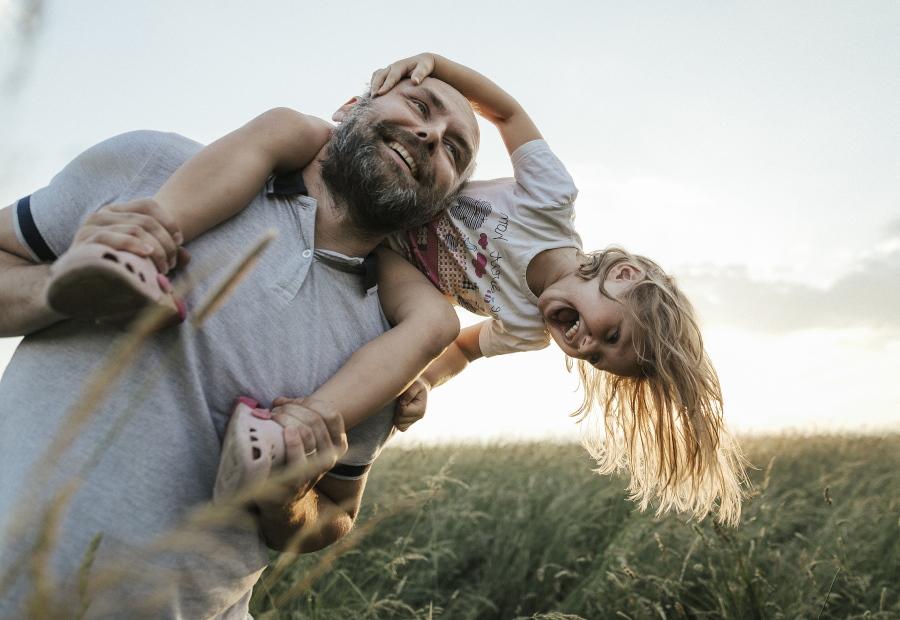 Kind lacht auf den Schultern des Vaters, im Hintergrund ist ein Windrad