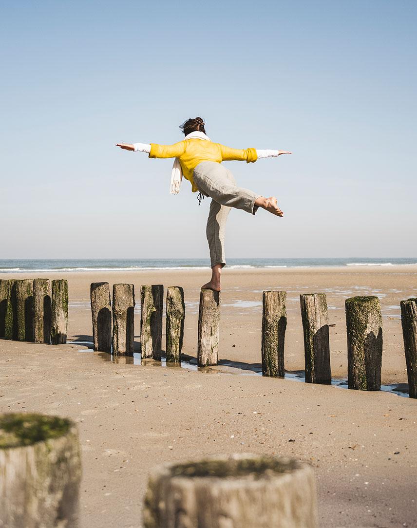 Frau balaciert schwankend auf einem Holzpfahl an der Nordseeküste